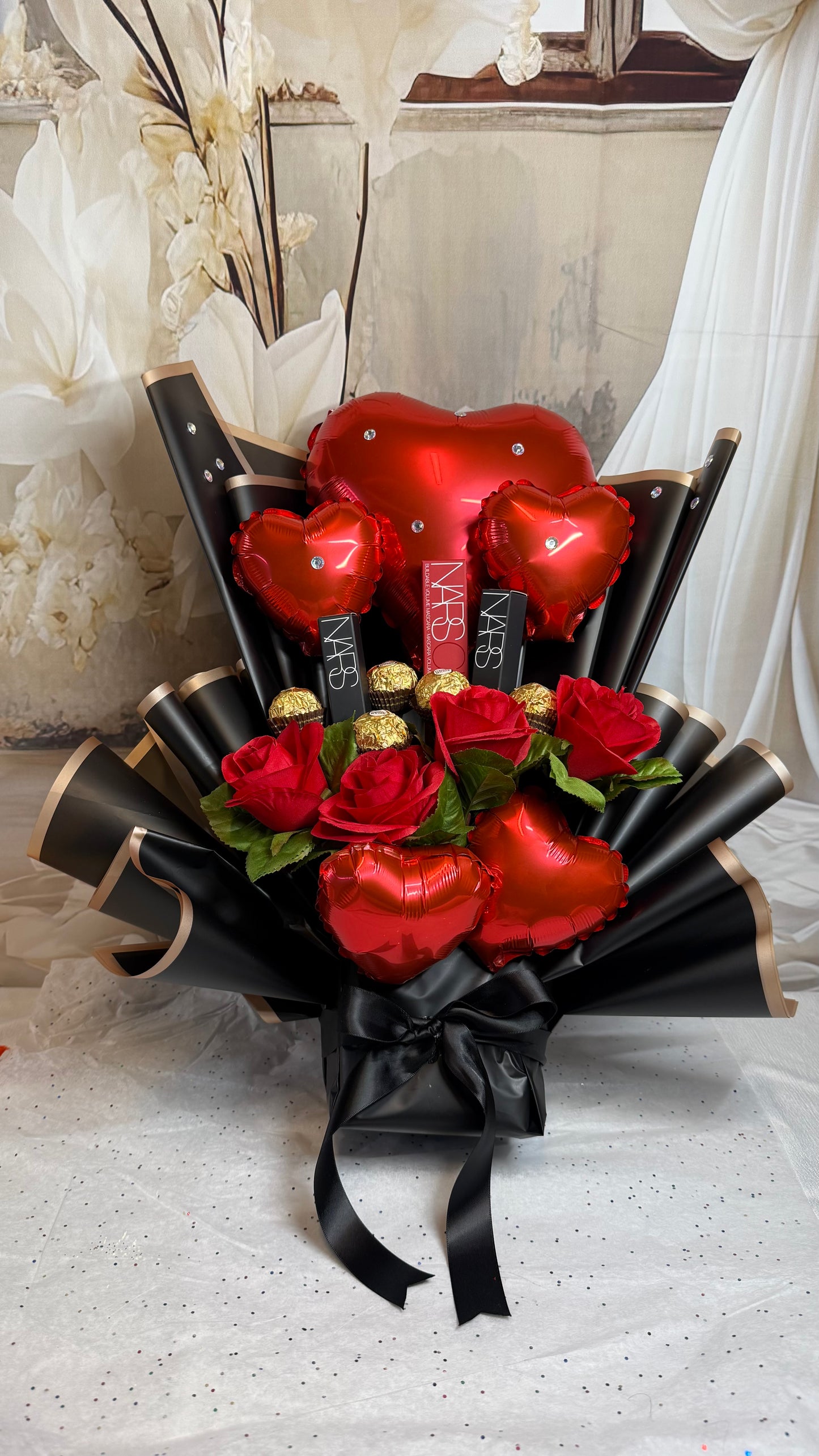 Bouquet of red roses and heart-shaped balloons with a black ribbon on a white surface.