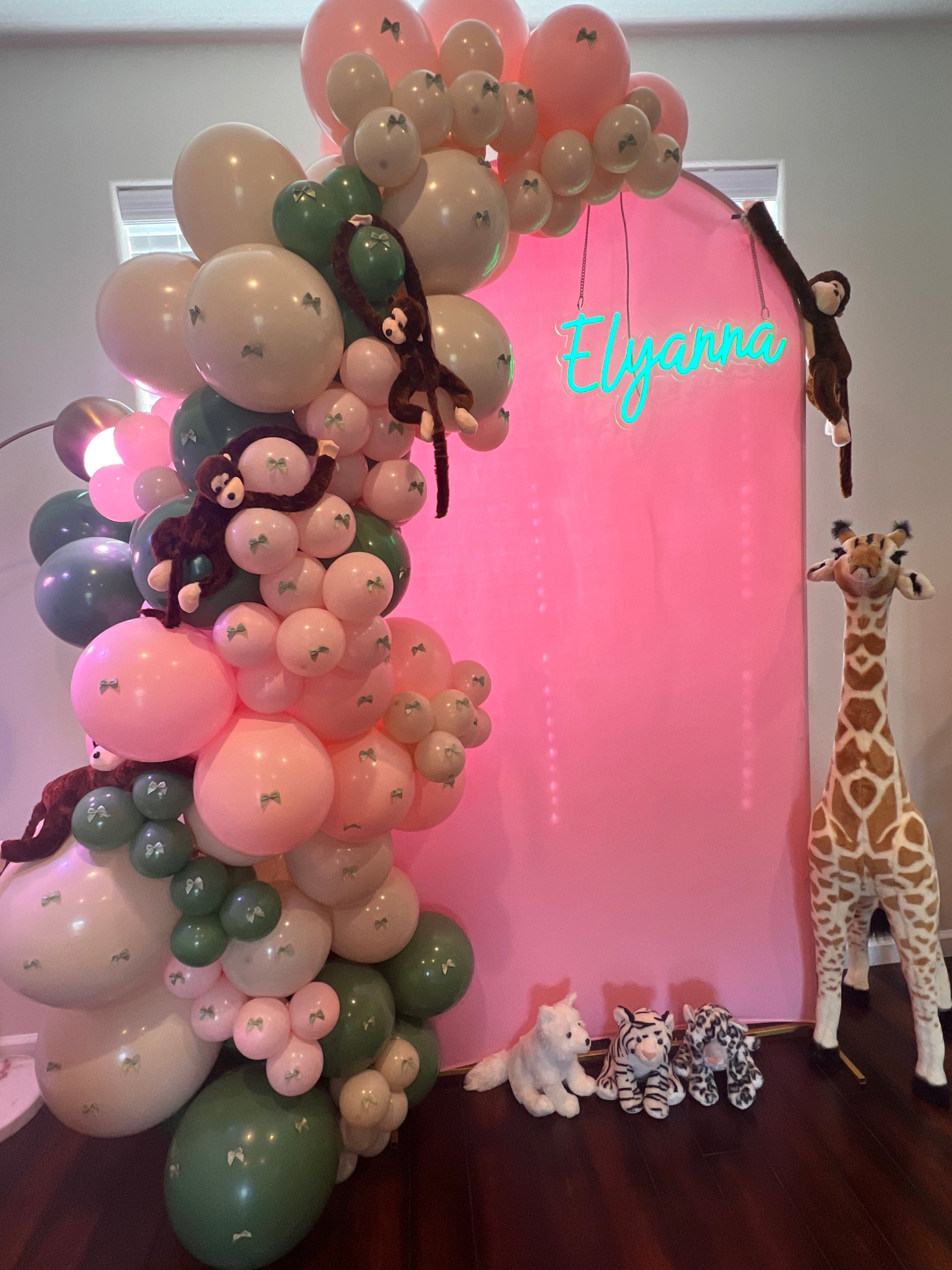 Balloon arch with pink, green, and white balloons, decorated with animal figures, against a plain background.