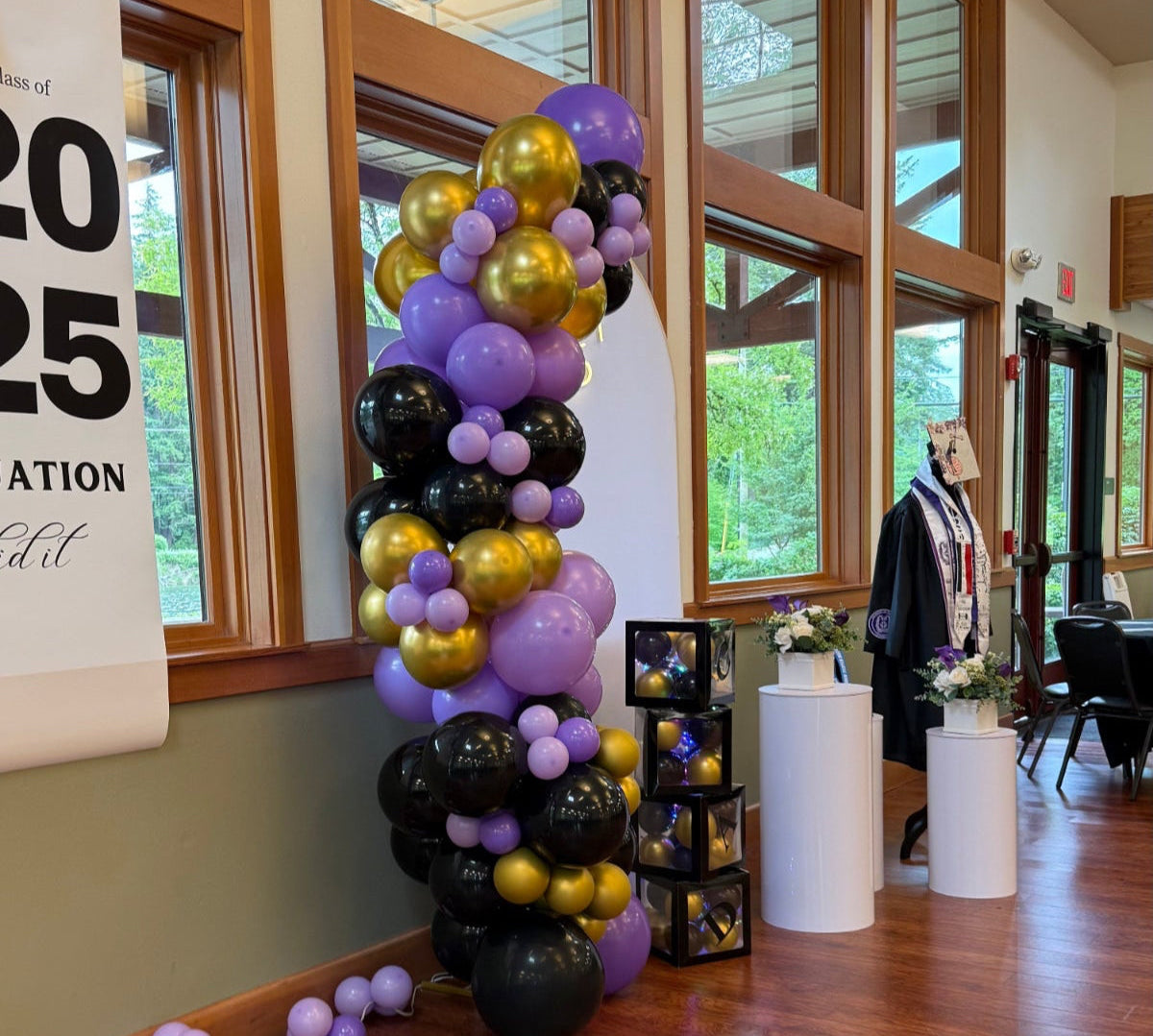 Graduation balloon arch in purple, gold, and black with cube balloon boxes and floral pedestals by Viola Art Decorations